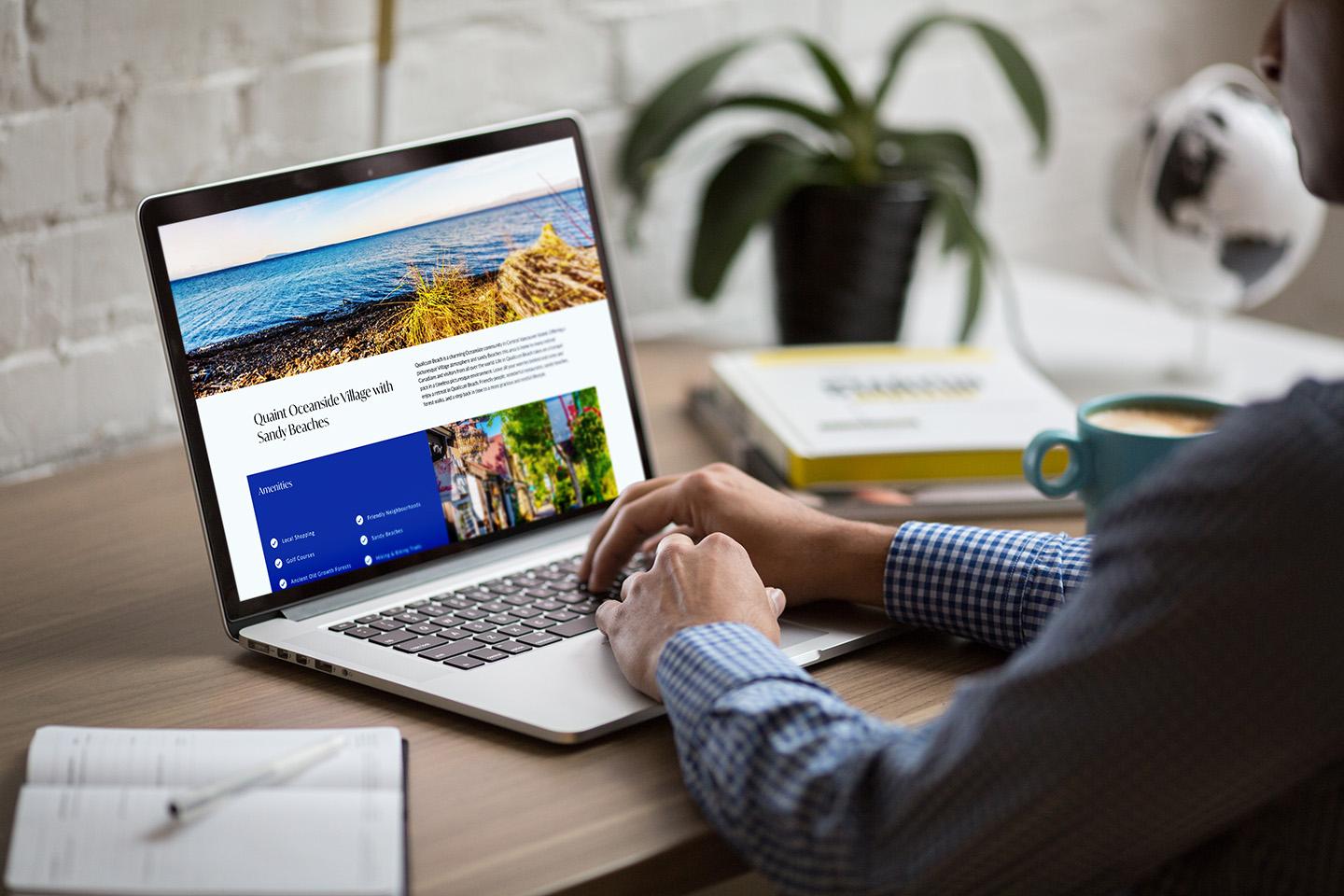 Karen Kenyon’s Qualicum Beach real estate and MLS® listings page displayed on a MacBook, showing local property details, neighborhood amenities, and scenic beachfront images. A person browses the website at a desk with a coffee mug, notebook, and plant, highlighting a modern home search experience.