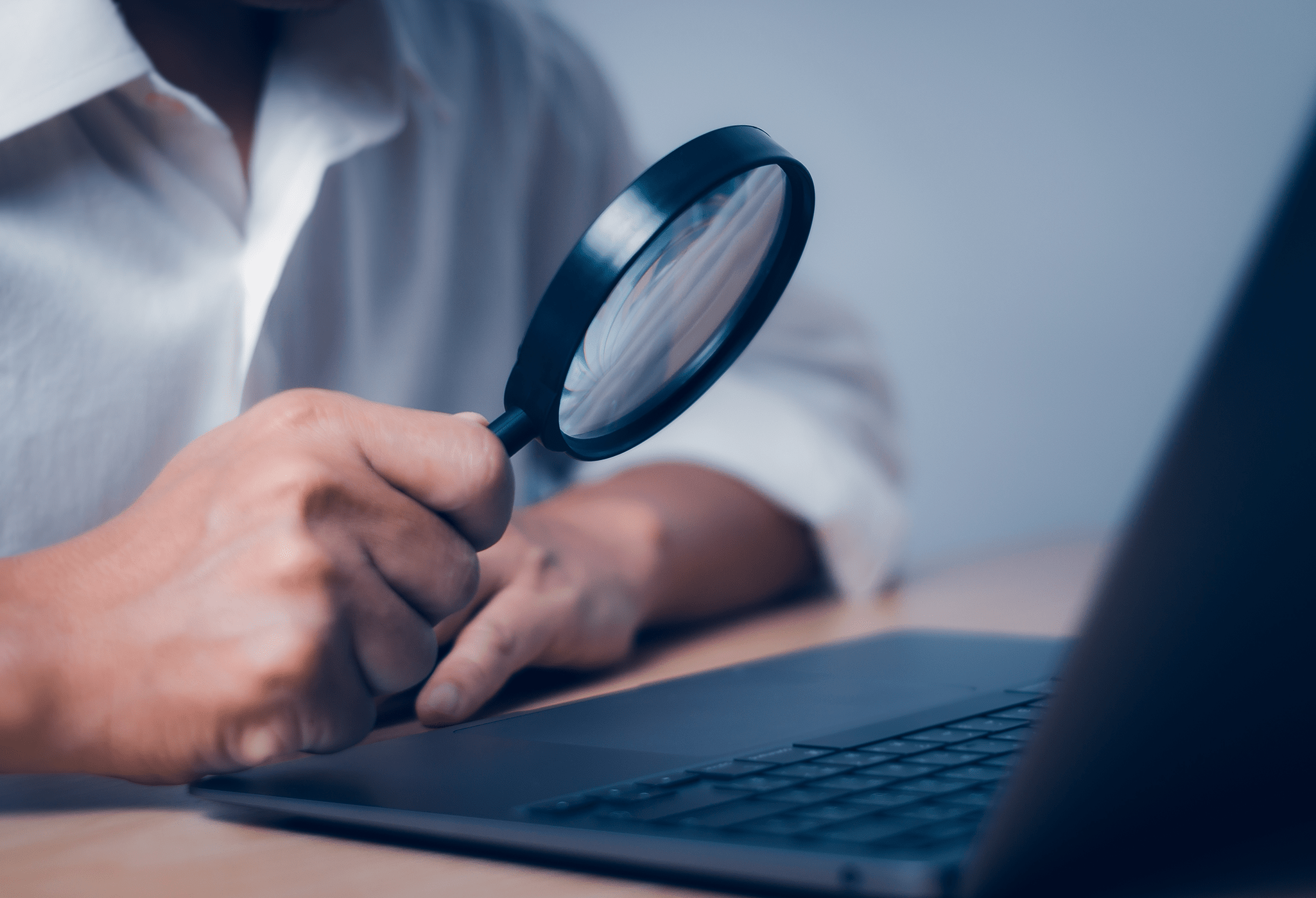 Person closely examining a laptop screen with magnifying glass, symbolizing high-intent real estate website visitors from organic search